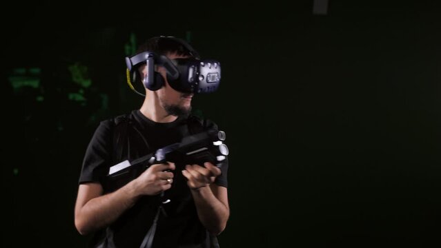 A man wearing virtual reality glasses is training with an automatic rifle in a dark room. Modern, futuristic entertainment.