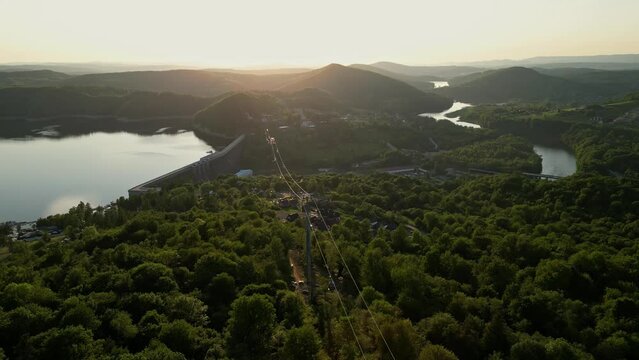 Panoramic view from the drone during sunset, on the Solińskie lake overlooking the modern gondola cable car with the lookout tower over the Solina water dam, in the Polish Bieszczady Mountains, Poland