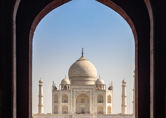 Fototapeta na wymiar A majestic Tajmahal, one of the world's seven wonders is viewed through its dark brown archways. A clear blue sky adds magnificence to the white marble of the beautiful architectural structure.