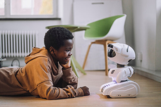 Smiling boy talking with AI robot while lying on floor in innovation lab