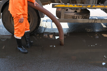 worker pumps out water with a special pump. cleaning of drains on the street. a man in an orange...