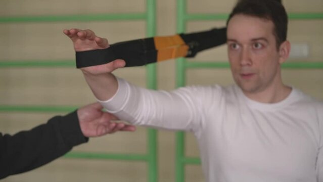 young caucasian man is engaged in strength fitness using TRX loops in the gym. a personal trainer helps an athlete train. close-up. slow motion video. High quality Full HD video recording