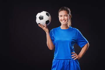  Portrait of young female smiling soccer player with soccer ball standing on isolated black Background.