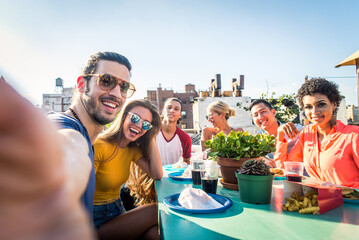 Multiethnic group of young happy friends bonding and having party at home on a rooftop terrace with...