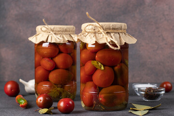 Homemade pickled tomatoes with chili peppers and parsley in glass jars on brown background