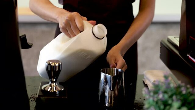 Woman barista hand provide milk to steam milk foam for hot cappuccino cup, staff or business trainee learning techniques to open coffee shop, close up hand pour milk into stainless cup