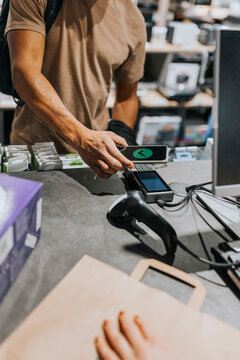 Midsection of male customer scanning credit card reader through smart phone at checkout in electronics store