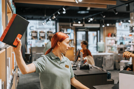 Redhead female sales clerk removing appliance from rack at electronics store