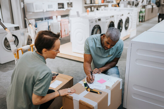 Saleswoman looking at salesman writing in document on box at appliances store
