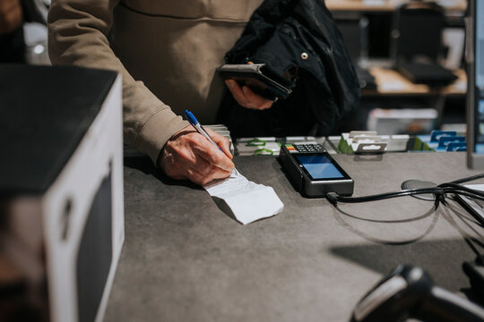 Midsection of senior man signing on bill by credit card reader at checkout in electronics store