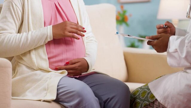 Close up shot of indian doctor counseling pregnant woman at home by taking asking and writing report - concept of pregnancy check up, medical treatment and health care.