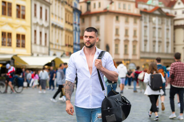 Travel concept. Male traveler with suitcase outdoor. Portrait of young caucasian man in shirt on summer vacation.