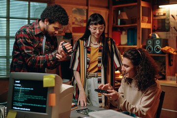 Guy shooting the working process on VHS camera while his colleague examining computer detail during their teamwork in garage