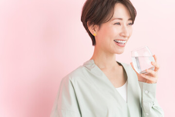 透明なグラスに入った水を飲む笑顔の日本人女性