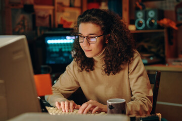 Young programmer in eyeglasses sitting at table in front of computer monitor and developing...