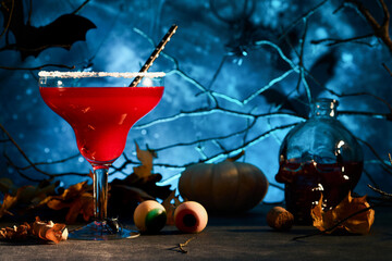 Halloween bloody cocktail margarita. Bloody red cocktail margarita   and bottle form skull on scary blue dark backgrounds. Festive drink for party with candy eyes, bats, spiders. Dia de los muertos.