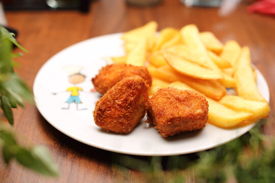Chicken nuggets with potato fries on a white plate, selective focus. Lunch, child portion.