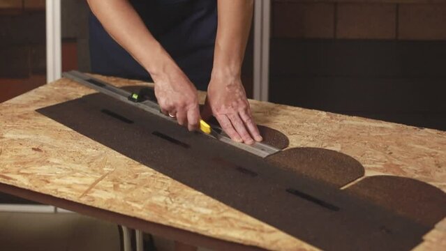 The process of cutting bituminous roofing tiles by a master indoors close-up
