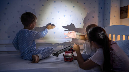 Happy kids with mother playing with flashlight in shadow theater at night