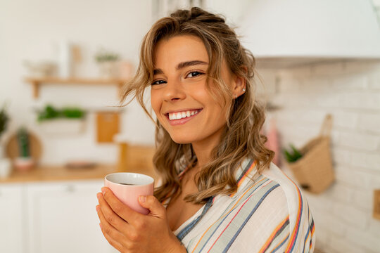 Young happy woman drinking coffee on the kitchen in the morning.