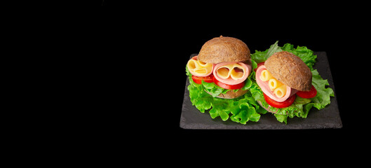 Delicious sandwiches with ham, tomatoes, cheese slices and fresh lettuce on black background with copy space. Banner