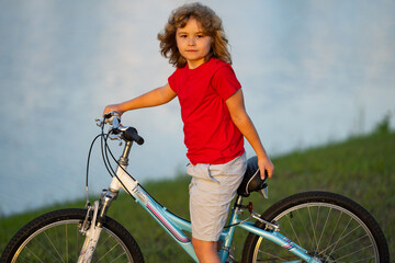 Fototapeta premium Child riding bicycle. Little kid boy on bicycle along bikeway. Happy cute little boy riding bicycle in summer park. Child cycling on bicycle. Kid riding bike.
