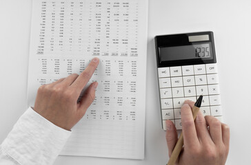 Woman using a calculator and points her finger at the numbers in the financial documents....