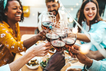 People clinking red wine glasses on rooftop dinner party - Happy friends eating meat and drinking...