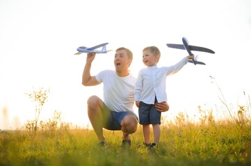 Cute little boy and his handsome young dad are smiling while playing with a toy airplane in the...
