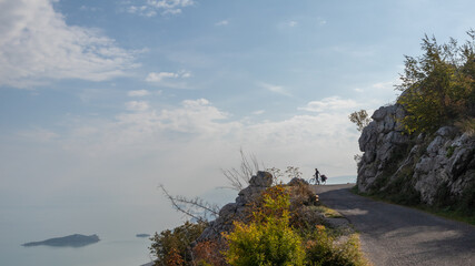 Cyclist standing on the side of mountain overlooking Lake Skadar in Montenegro. 