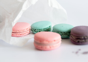 Multi-colored macarons falling out of white paper bag