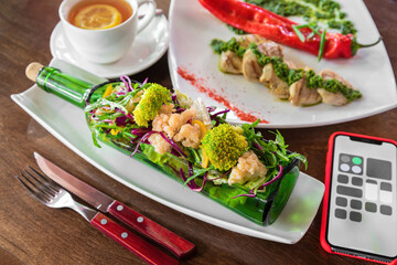 Green vegan salad in glass win bottle with some tea. Top view on wooden table.