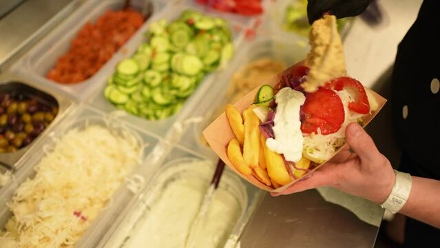 Process of preparing a kebab fast food putting the white sauce and hummus on a plate with fries and vegetables in