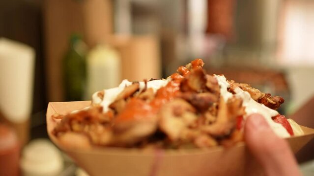 Pouring red sauce on top of a take away gyros shawarma plate close-up