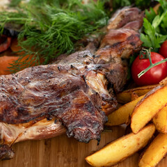 Fried meat with side dish of potatoes and vegetables. Dish on wooden board. Lamb with vegetables. Wooden background. View from above. Close-up. Soft focus. 