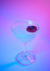 Tasty, sweet alcohol cocktail, Margarita glass with slice of dry orange over pink gradient background in neon glow. Party club entertainment. Mixed light