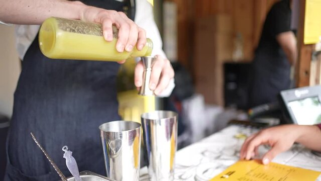 Cocktail bartender pouring yellow pineapple juice into a shot glass to shake and mix