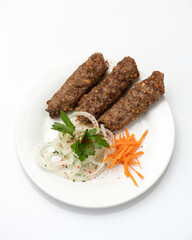 Three kebabs with spices and vegetables on white round plate. Fried kebab with onions and carrots. Asian, Turkish cuisine. White background. View from above. Copy space.