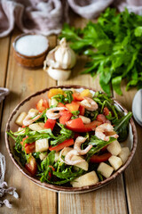 Delicious dish for a romantic lunch or dinner: salad with shrimp, sweet pepper, arugula, juicy pear, tomatoes, garlic and olive oil in a beautiful plate on wooden boards. Vertical photo