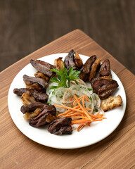Liver skewers with carrots and onions on a white plate. Pieces of fried liver with bacon and vegetables are decorated with parsley. Middle Eastern cuisine. Wooden background. Top view. Copy space.