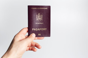 Close-up of male hand holding Romanian passport in hand on white background.