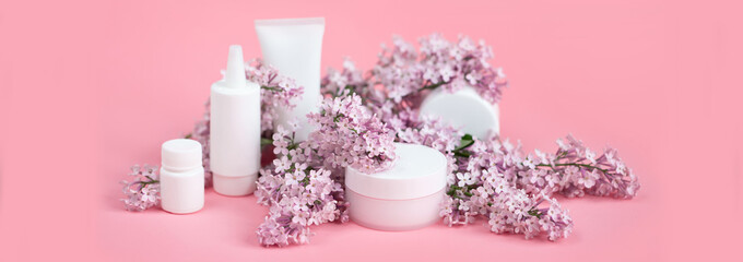 Face and body skin care. A set of cosmetic creams and balms in white tubes and cans on a coral background with sprigs of lilac flowers. Spa treatments for home care. Home rejuvenation and moisturizing