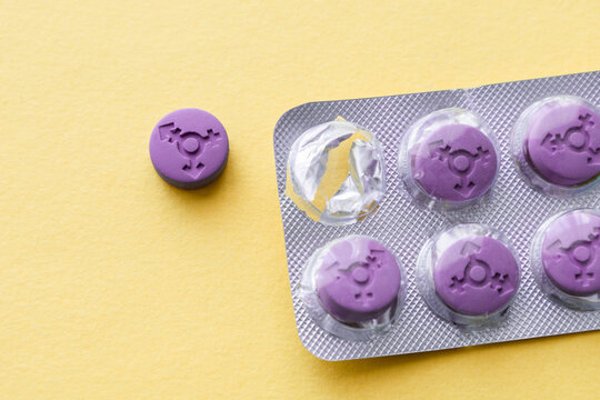 Purple pill with a transgender gender symbol in a blister on a yellow background. Hormonal pills