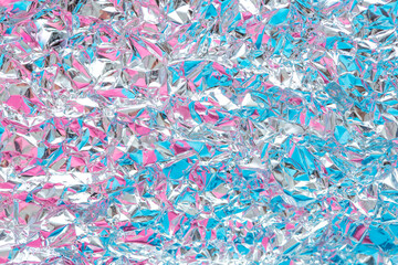 The surface of the crumpled foil is highlighted in different colors. Background holographic iridescent multicolored texture.
