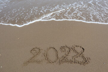 New Year 2028 written in the sand on a beach with sea wave background.