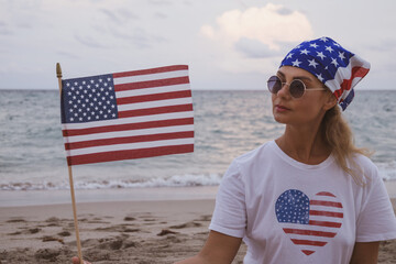 The girl is sitting on the beach with the American flag. Patriotism. Girl on the beach. Independence Day