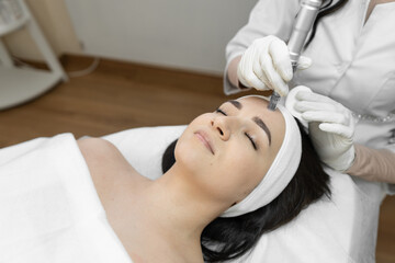 Obraz na płótnie Canvas A professional cosmetologist uses innovative fractional mesotherapy to improve the condition of the skin in a beauty salon. The young woman is relaxed and rests during cosmetic procedures.