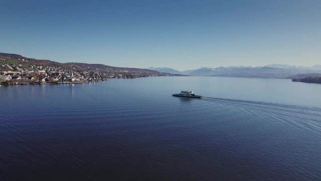 Aerial panoramic drone view of the Horgen to Meilen ferry crossing Lake Zurich, and local church, Reformierte Kirche Meilen, with Swiss Alps in the background, Switzerland