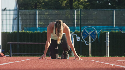 Caucasian woman at the athletic track starting point, hands on the start line and legs on starting...