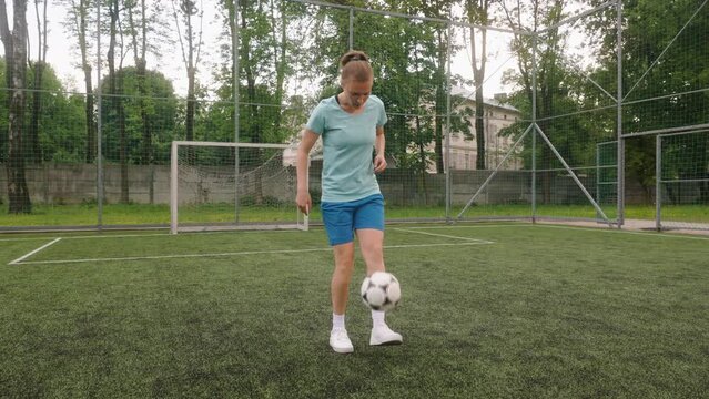 The female football player is training on a mini-football field with artificial turf. Professional footballer lifts the ball with her feet from the floor and skillfully juggles it kicks up on foot.